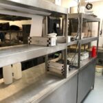 Stainless steel preparation counter with twin-tiered overhead shelving.