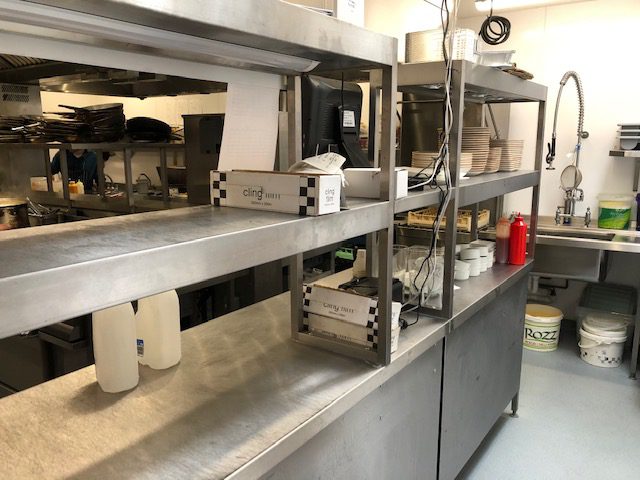 Stainless steel preparation counter with twin-tiered overhead shelving.