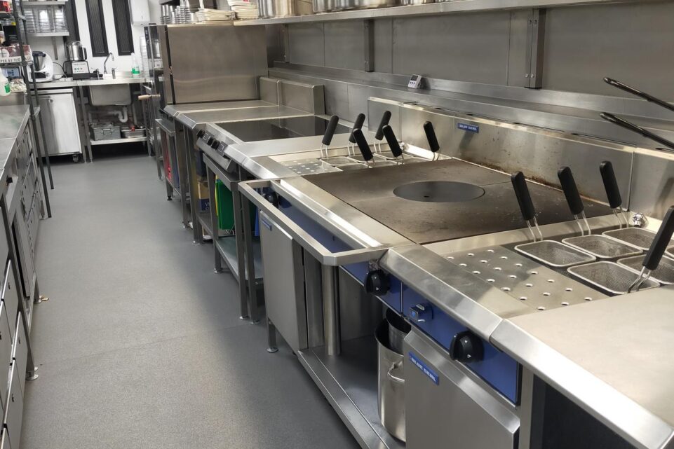 Commercial kitchen cooking line, featuring a long custom-fabricated stainless steel suite of equipment.