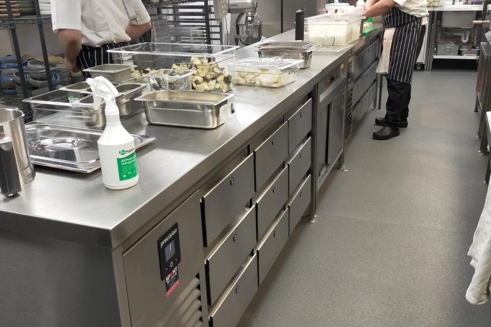 Commercial kitchen preparation area during service, showing a chef working at a long stainless steel counter